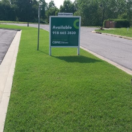 A plot of grass outlining a commercial parking lot. The grass is mowed and carefully maintained by Sprague's Kik'N Grass.