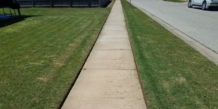 An image of a sidewalk. The surrounding grass has been mowed and sides have been edged.
