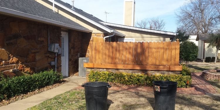 A backyard with a small fence. Both the home and fenced are lined with small shrubs that have been neatly pruned.